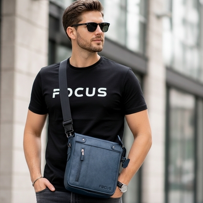 Man wearing a black 'FOCUS' t-shirt and sunglasses, holding a blue crossbody bag in an urban setting.