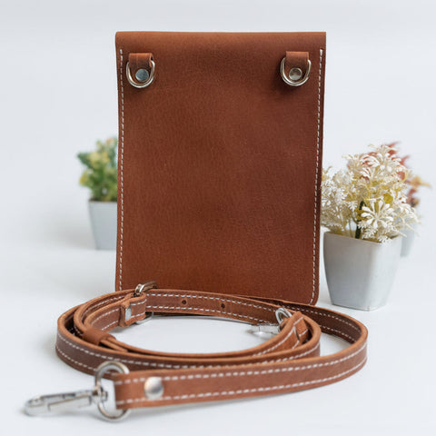 Brown leather crossbody bag with strap on a light gray background