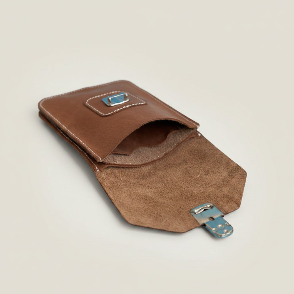 Brown leather pouch with metal clasp on a gray surface with a blurred plant in the background