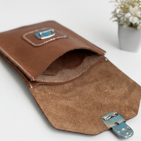 Brown leather pouch with metal clasp on a gray surface with a blurred plant in the background