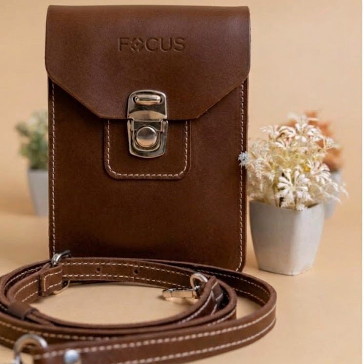 A brown leather pouch bag with a flap closure and silver metal clasp, shown with a matching brown strap on a beige background. The brand name 'FOCUS' is embossed on the front flap.