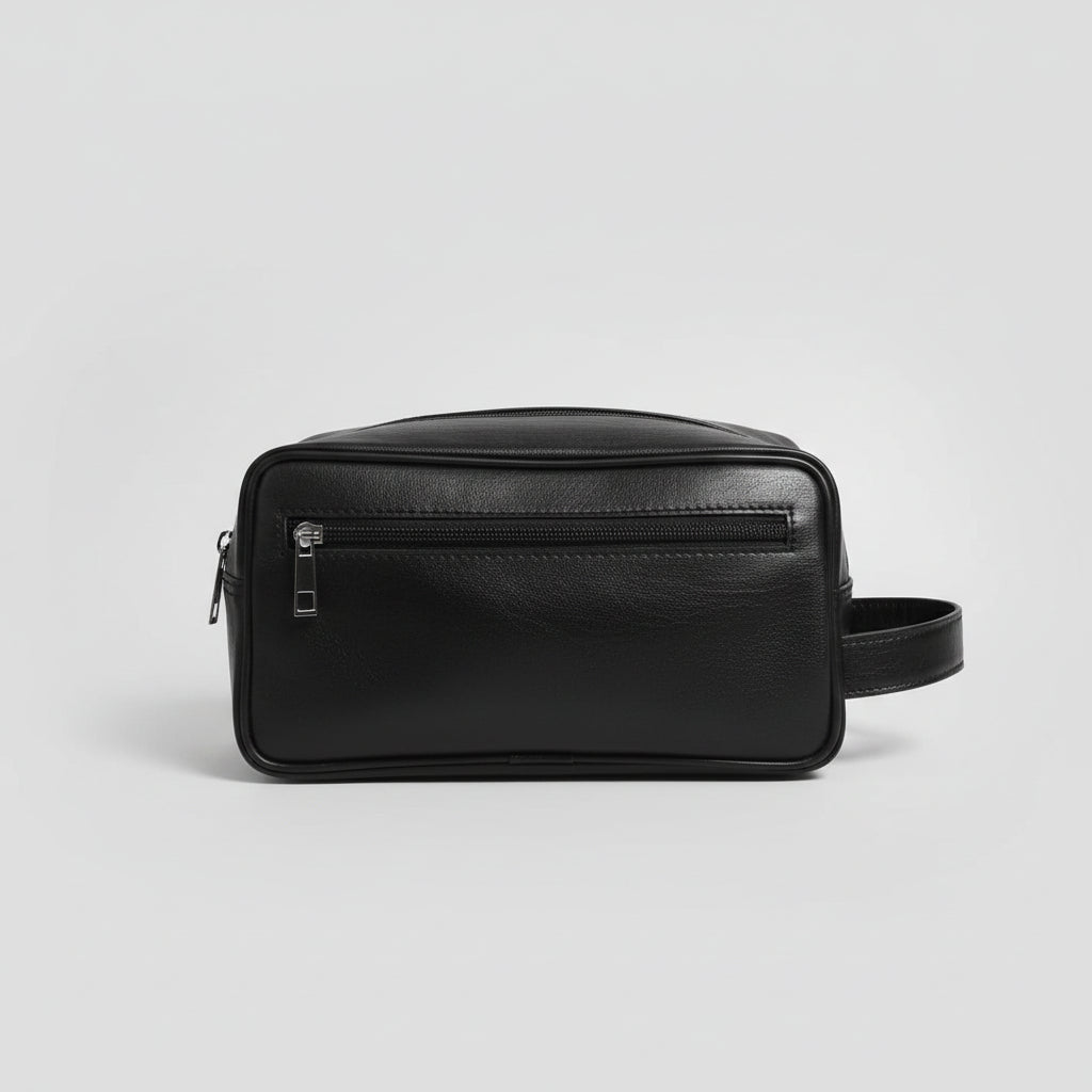 A black faux-leather rectangular pouch bag with a front zippered pocket and a side handle, resting on a glass table in an indoor setting.
