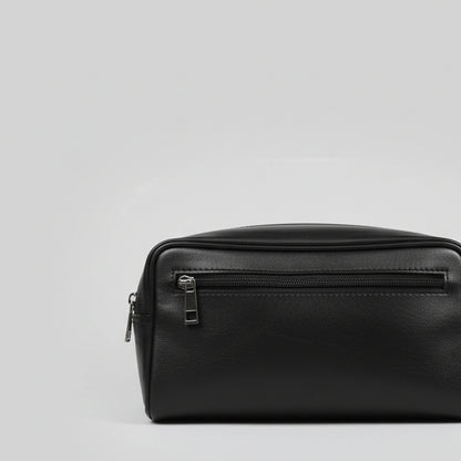 A black leather zippered pouch or small bag with a silver zipper pull, photographed on a reflective glass tabletop.