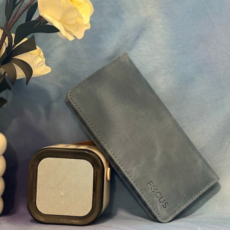 Gray wallet and square speaker on a light blue surface with yellow flowers in the background