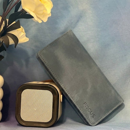 Gray wallet and square speaker on a light blue surface with yellow flowers in the background